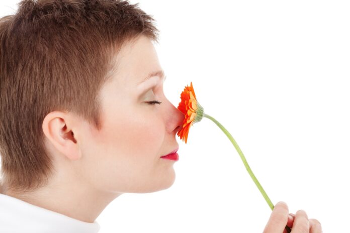 Frau mit kurzen Haaren riecht an Blume