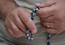 Mann betet mit Rosenkranz in der Hand