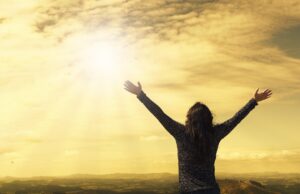 Frau streckt ihre Hände dem Himmel und dem Sonnenlicht entgegen