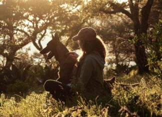 Frau sitzt mit ihrem Hund am Waldrand
