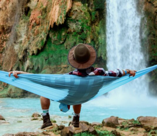 Mann liegt völlig entspannt in einer Hängematte vor einem Wasserfall
