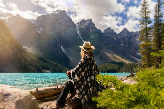 Frau sitzt in der Natur und genießt die Aussicht auf den See und die Berge