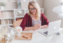 hübsche blonde Frau sitzt mit Brille vor Laptop und macht Home Office