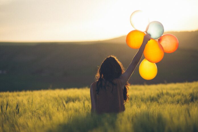 Frau mit Luftballons in der Hand steht in einem Feld