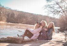 3 attraktive Frauen sitzen strahlend lächelnd an einem Flussufer