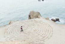 Mann geht an einem Strand in ein kreisförmiges Labyrinth