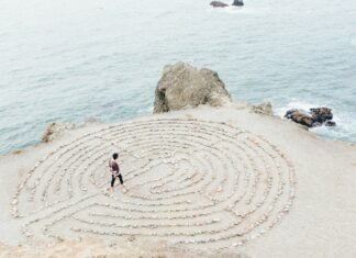 Mann geht an einem Strand in ein kreisförmiges Labyrinth
